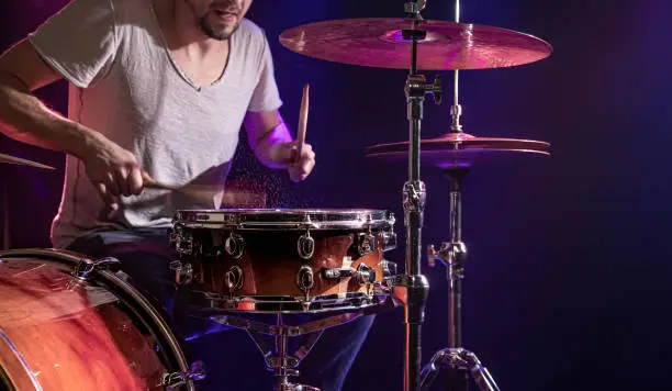 Photo of The drummer plays the drums. Beautiful blue and red background, with rays of light. Beautiful special effects smoke and lighting. The process of playing a musical instrument. Close-up photo.