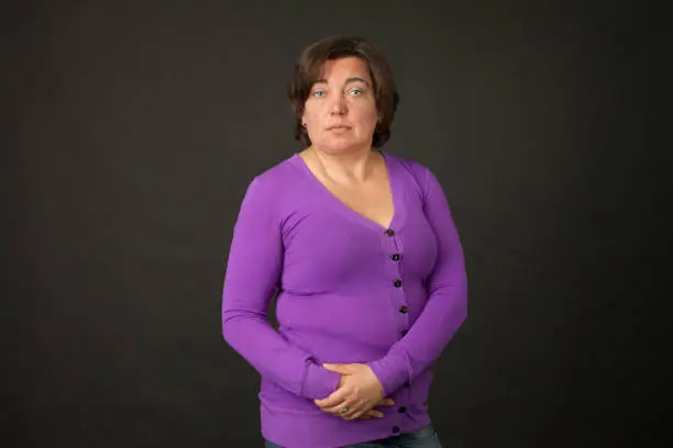 Close-up studio portrait of a 40 year old woman in purple cardigan on black background