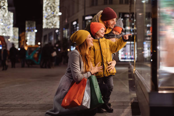 Family with two kids in front of the store window Family with two kids in front of the store window in a big city at night kids winter coat stock pictures, royalty-free photos & images