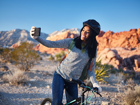 fit african american woman taking a break from riding bike to use smartphone for selfie  during the day