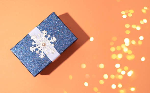 istock Blue shiny Christmas gift with snowflake on orange background. A festive composition. 1195308044