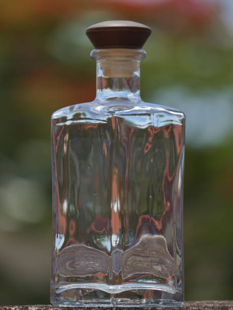 istock Transparent glass bottle reflecting sunlight with defocused treetops in the background. 1195320733