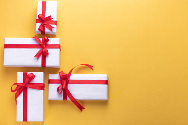 White gift box with red ribbon, light coloured background flat lay for stock image