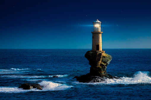 Light beam of the south stack lighthouse, near Holyhead in Wales, moving over the stormy coastline at dusk. Beautiful contrast of the warm light from the lighthouse to the blue-cold surrounding. Wales, UK