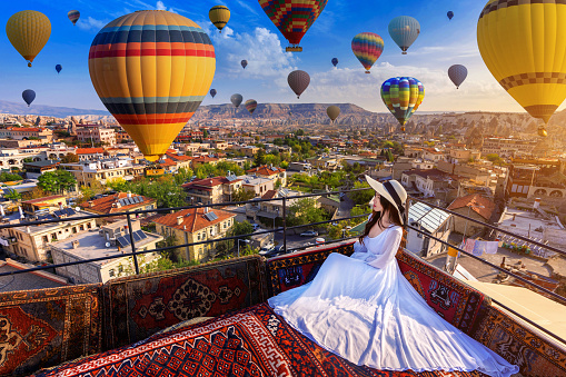 Beautiful girl sitting on the hotel and looking to hot air balloons in Cappadocia, Turkey.
