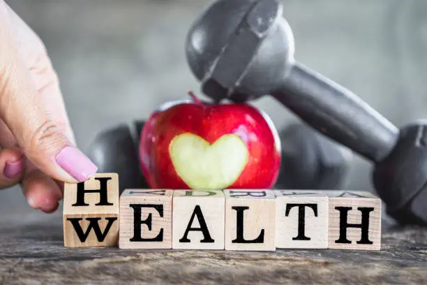 Photo of hand flipping word health to wealth with red apple and dumbbells