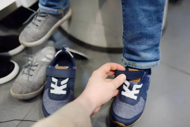 Photo of Little boy during shopping with his mother. Kid trying new fashion seasonal sneakers.
