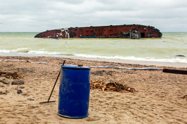 istock fighting the consequences of a tanker wreck on a sandy beach a protective barrier and a barrel for collecting oil waste. 1195383904