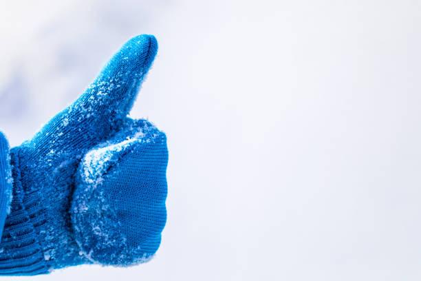 Thumb up in blue mitten, cool sign, snow background