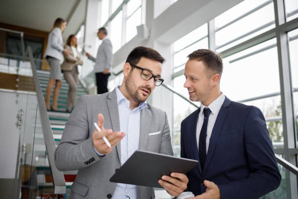 istock Two businessmen sharing corporate ideas using a digital tablet in office lobby 1195386985