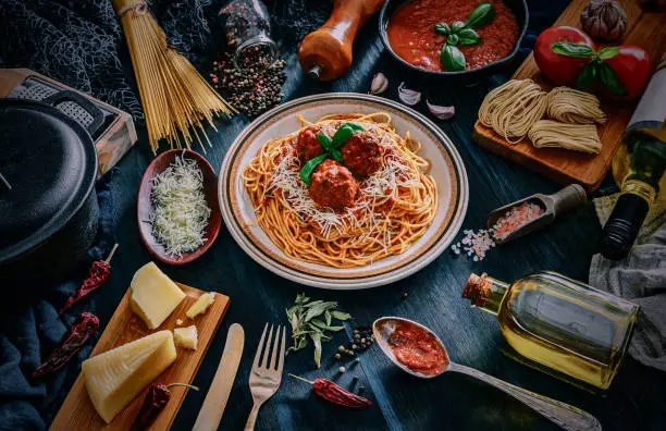 Spaghetti with meatballs and and ingredients on rustic pots. Shot taken on wooden bluish table in rustic kitchen