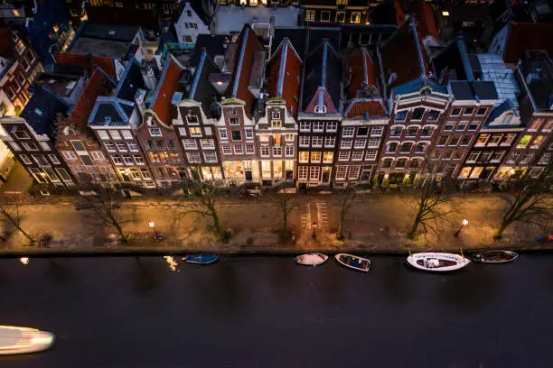 Aerial views of the Dutch capital, Amsterdam at night. Tall houses on the banks of canals with tourist boats exploring the hundreds of rivers crossing through the city.