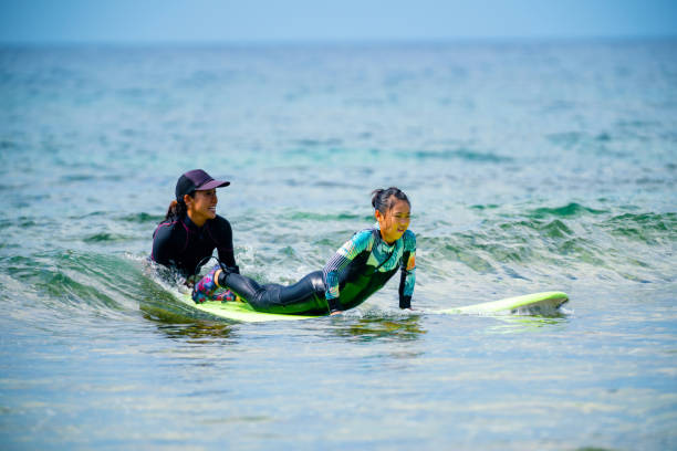 Teenage girl taking a surfing lesson from her mother stock photo