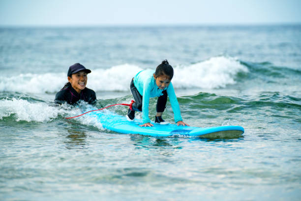 istock Mother teaching her young daughter how to surf during a tropical vacation 1195393529