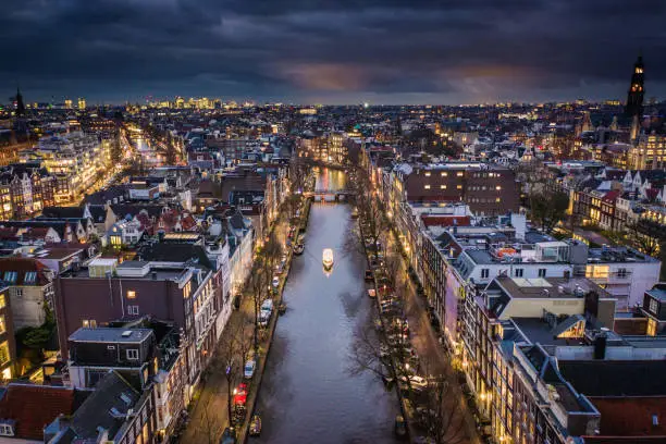 Aerial views of the Dutch capital, Amsterdam at night. Tall houses on the banks of canals with tourist boats exploring the hundreds of rivers crossing through the city, a popular tourist destination in Europe.