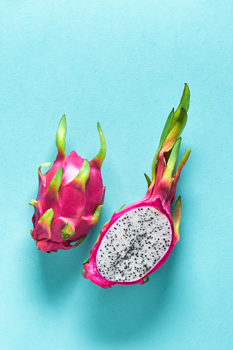 Creative flat layout with fresh organic pink, white and green dragonfruit (pitaya or pitahaya) on blue mint paper background. Trendy top view, flat lay view of the fruit cut in half.