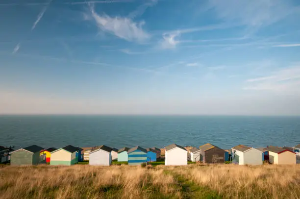 Colourful holiday wooden beach huts facing the calm Atlantic sea agains a blue cloudy sky.  Whitstable at Kent Great Britain