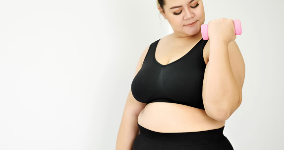 Chubby woman doing exercise by dumbbell in a room.