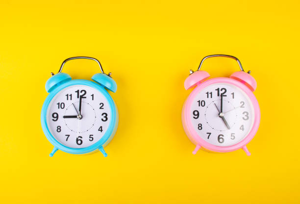 two alarm clocks on a bright yellow background showing different time - 5 horas imagens e fotografias de stock