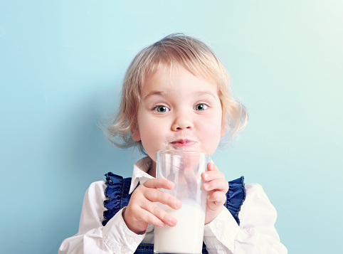 Cute caucasian toddler child with glass of milk portrait on blue background.Healthy kid's nutrition.Retro design.