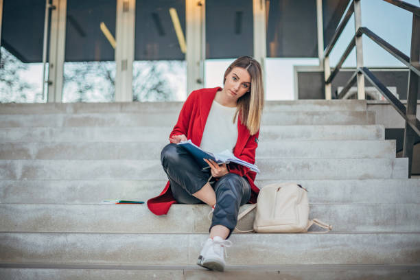 A student girl on campus is sitting on the stairs and using a smartphone while waiting for classes to begin. Back to school concept