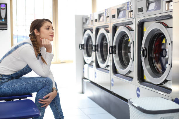 Young woman at a laundromat, sitting on a chair and waiting. About 25 years old, Caucasian female.