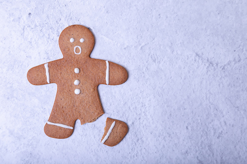 A ginger man with a broken leg (no leg) and a surprised face. Traditional Christmas and Christmas homemade cookies. Selective focus, close-ups. Space for text.