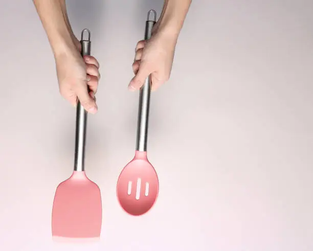 Hands holding silicone shpatula for cooking with metal handle on a gray background. Top view."n