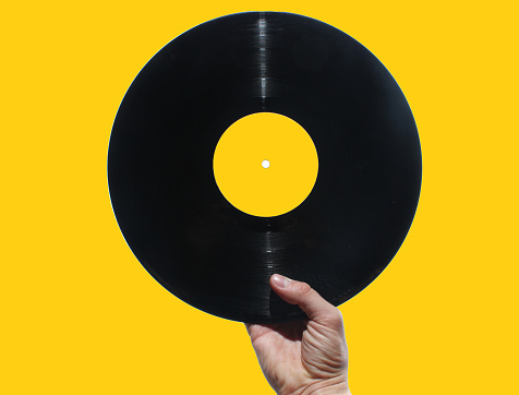 Hand holding vinyl record isolated on yellow, retro style