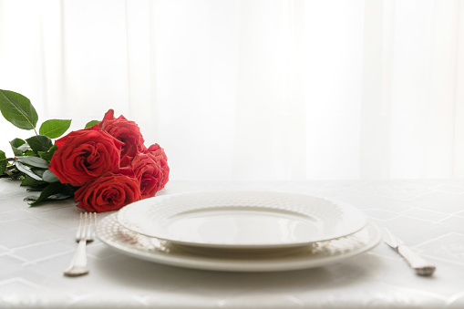 Romantic table place setting with bouquet red roses. Space for text. Invitation for date. Valentines day