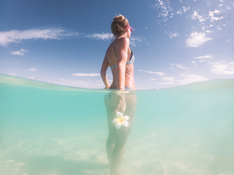 Half split underwater shot view of woman enjoying pristine clear water beach in Hawaii looking up