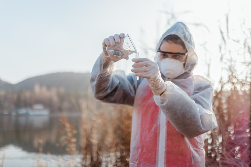 Female biochemist or infectious disease specialist conducts a chemical test of water against the background of a sewer with leaking water