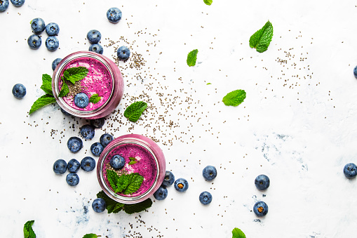 Purple smoothie with blueberries, chia seeds and mint leaves in glass jars on white background, flat lay, top view