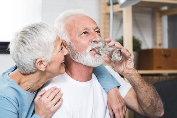 Senior couple drink water Happy beautiful senior man, white beard and grey hair,  holding transparent glass in his hand and drink water. Smiling wife near by. Concept healthy life and diet for senior people. Closeup. old man pajamas photos stock pictures, royalty-free photos & images