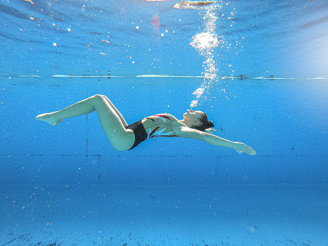 Synchronized swimming performance of a young woman practicing an act underwater in a swimming pool.