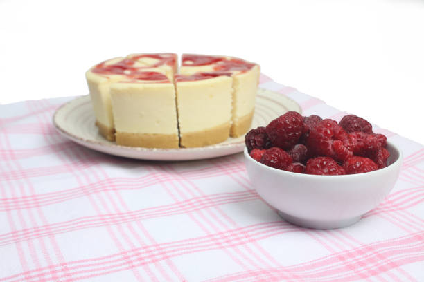 cheesecake on a plate and a bowl of raspberry on red and white tablecloth