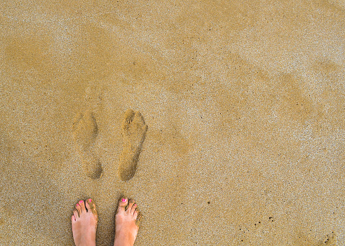 Horizontal looking down to barefoot walking in sand along shoreline water at Australian seaside coastal town Byron Bay NSW Australia