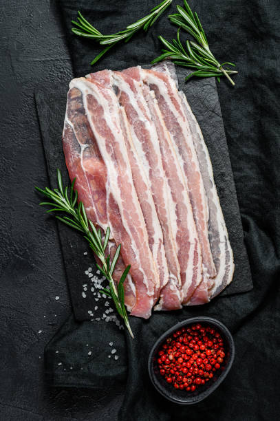 istock Raw bacon on a stone chopping Board. Pork meat. Black background. Top view 1195441722