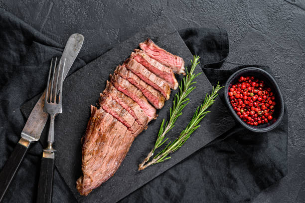 istock Steak of marbled beef roasting medium on a black stone Board. Black background. Top view 1195444300