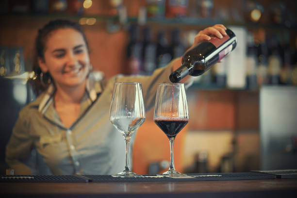 istock Girl bartender pours red wine into two wine glass 1195448924