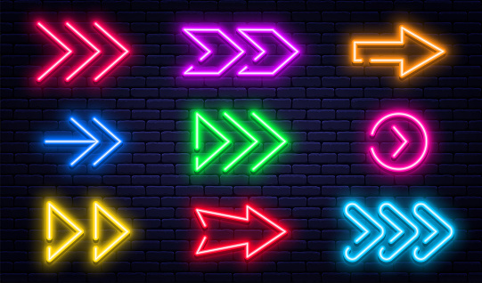 Set of glowing neon arrows. Glowing neon arrow pointers on brick wall background. Retro signboard with bright neon tubes in red, yellow, purple and blue colors. Vector