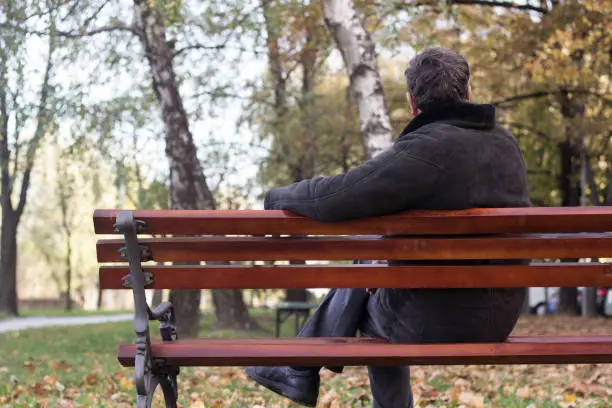 Portrait of a pensive senior man sitting on the bench, in the public park, outdoors. Old man relaxing outdoors and looking away. Portrait of elderly man enjoying retirement