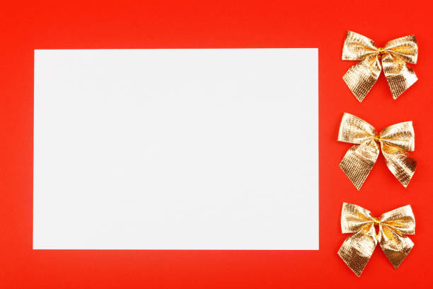 istock Blank white paper with golden holiday bows on red background 1195467397