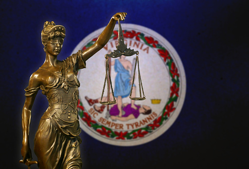 Close-up of a small bronze statuette of Lady Justice before a flag of Virginia.