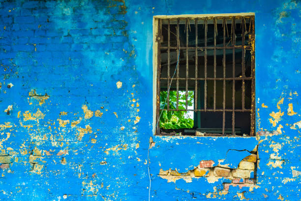 Abandoned vintage brick wall building with rotting metal burglar bars on window opening and stripping blue surface paint Abandoned vintage brick wall building with rotting metal burglar bars on window opening and stripping blue surface paint on facade. Forgotten old business property with cracked walls, falling apart. falmouth harbor stock pictures, royalty-free photos & images