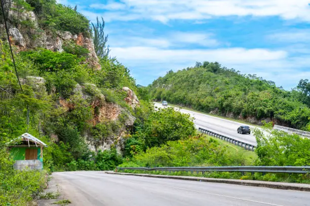 Highway through the mountain countryside. Vehicles driving in opposite directions on asphalt/ concrete bypass road/ roadway/ street. Lush greenery through tropical Caribbean island hills.