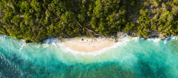 View from above, stunning aerial view of some tourists sunbathing on a beautiful beach bathed by a turquoise rough sea during sunset, Topan Beach, South Bali, Indonesia. View from above, stunning aerial view of some tourists sunbathing on a beautiful beach bathed by a turquoise rough sea during sunset, Topan Beach, South Bali, Indonesia. bali stock pictures, royalty-free photos & images
