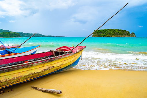 Colorful old wooden fishing boats docked by water on a beautiful beach coast. White sand sea shore landscape on tropical Caribbean island. Holiday weekend/ summer vacation setting in Jamaica.