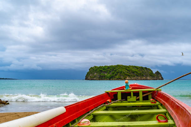 toy doll sitting in front colorful old wooden fishing boat docked by water on beautiful beach coast sea shore landscape on tropical caribbean island - cabarita beach imagens e fotografias de stock