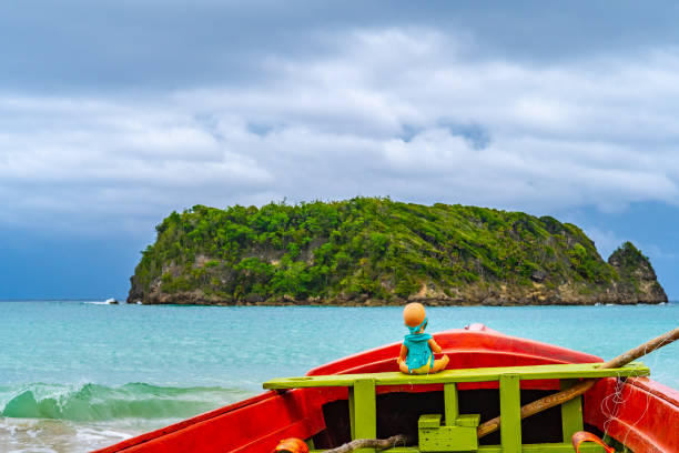 toy doll sitting in front colorful old wooden fishing boat docked by water on beautiful beach coast sea shore landscape on tropical caribbean island - cabarita beach imagens e fotografias de stock